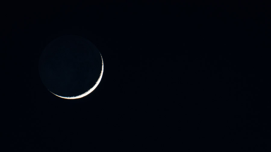 A thin crescent moon glowing sharply against a black night sky