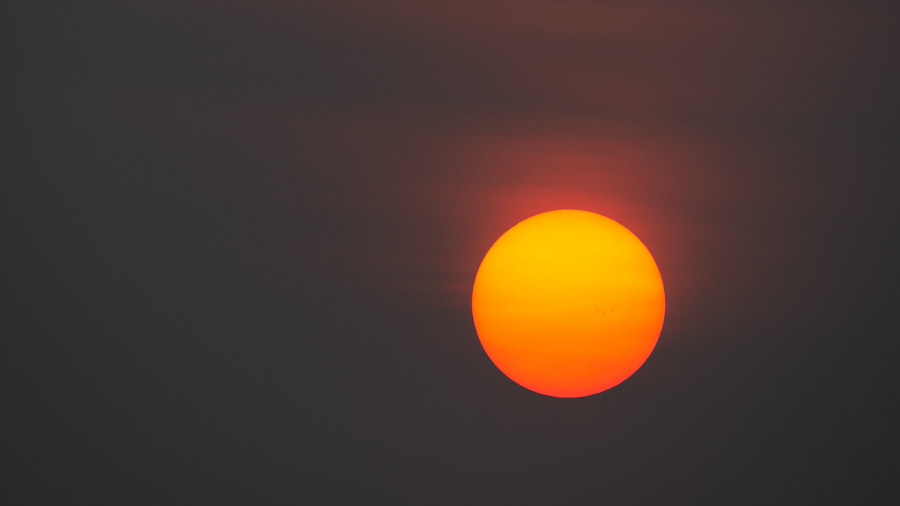 The sun reduced to a dim orange disc behind a flat grey sky of wildfire smoke